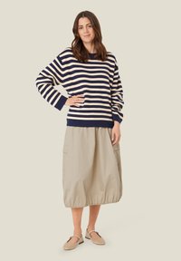 Gestreifter Pullover in Marineblau und Creme, kombiniert mit einem beigen Ballonrock. Der Pullover hat weite Ärmel und gerippte Bündchen.