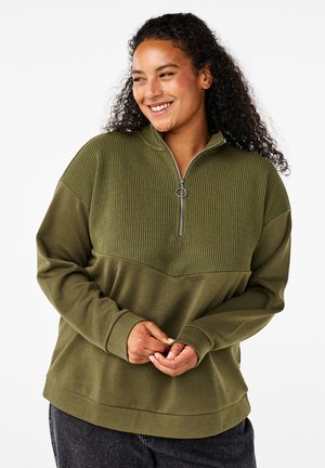 Pullover verde oliva con mezza zip realizzato in tessuto testurizzato, con un motivo a costine nella parte superiore e una sezione inferiore liscia.