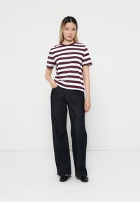 Camiseta a rayas en burdeos y blanco, de mangas cortas, combinada con unos jeans de mezclilla oscuros de talle alto, modelo de pie contra un fondo liso.