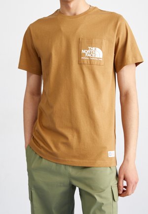 Bruine katoenen t-shirt met ronde hals en korte mouwen, met een wit logo op de borstzak. Gecombineerd met groene cargo broek.