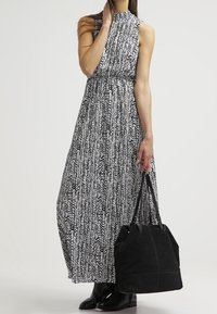 Long black and white patterned sleeveless dress with a gathered waist, paired with a black tote bag and knee-high black boots.