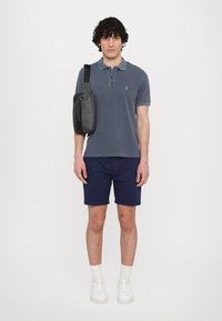 Polo de bărbați de culoare bleumarin, din amestec de bumbac, cu mânici scurte și accente gri. Este purtat cu pantaloni scurți bleumarin și adidași albi, având asupra lui o geantă crossover neagră.