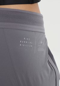 Gros plan sur la taille et la hanche portant un short gris Nike Running Division avec une ceinture en mesh et un texte imprimé sur le tissu.