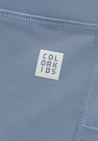 Ljusblått tyg med en vävd textur och en vit fyrkantig etikett med "COLOR KIDS" tryckt i blockbokstäver.