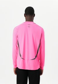 Long-sleeve athletic shirt in bright pink, featuring black accents and a circular logo on the back near the neckline. Smooth texture.