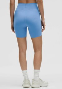 Shorts atletici cu talie înaltă, de culoare albastră, cu o textură netedă. Prezintă un design ajustat și un elastic fără cusături. Asortați cu sosete albe și adidași.