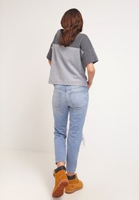 Grijs cropped topje met korte mouwen, gecombineerd met lichtblauwe verfrommelde jeans en bruine laarzen met een zwarte kraag en een robuuste zool.