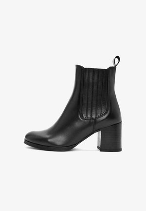 Bottine en cuir noir avec des panneaux élastiques sur les côtés, bout arrondi et un talon bloc texturé. Elle est dotée d'une languette pour un enfilage facile.