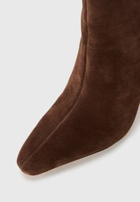 Brown suede ankle boot with a pointed toe, smooth texture, and seamless design, showcasing rich color and elegant silhouette.
