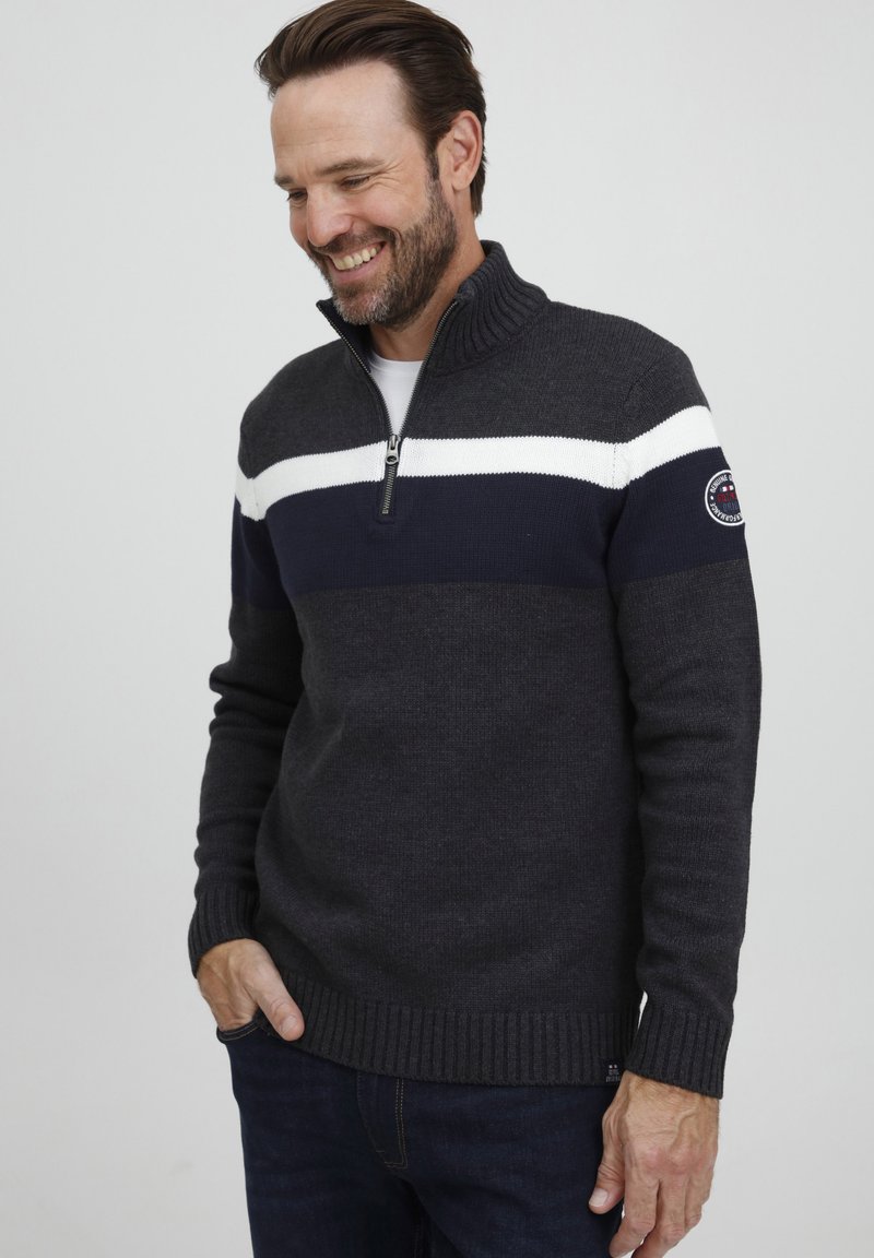 Maglione grigio scuro con zip e collo a costine, caratterizzato da una striscia bianca e blu navy sul petto e un piccolo logo sulla manica.