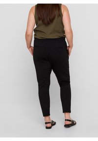 Svarta tapered byxor med elastisk midja, sidofickor och en mjuk textur, tillsammans med en mörkgrön ärmlös topp.