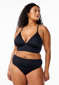 Curly-haired woman wearing black two-piece swimsuit, looking to her left against a plain white background.