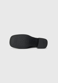 Semelle de chaussure en caoutchouc noir avec un motif de texture antidérapant et un talon lisse. Bout arrondi et arrière légèrement surélevé pour le soutien.