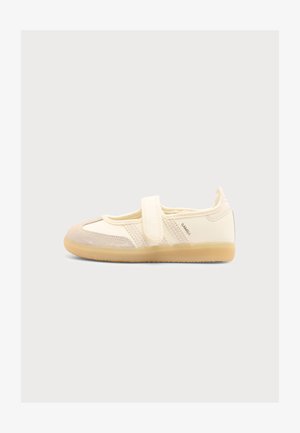 Børnesko i cremefarve med beige ruskindstå, velcrolukning og gennemsnitlig gummisål, vist fra siden på en ensfarvet baggrund.