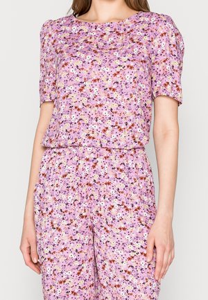 Mujer con conjunto a juego de top de manga corta y pantalones con fondo rosa y pequeño estampado floral multicolor.