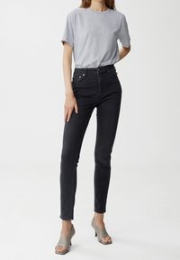 Höga svarta denimjeans med slim fit, uppvisade med en grå t-shirt och grå öppna klackar mot en neutral bakgrund.