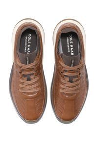 Sneaker in pelle marrone perforata con dettagli texturizzati, lacci marroni e una suola bianca a contrasto. Logo del marchio visibile sulle sole interne.