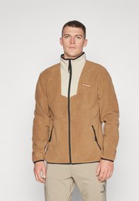 Brun fleecejakke med en lys beige frontpanel, høj krave, fuld lynlås og sidelommer, med en sort lynlås og brandlogo.