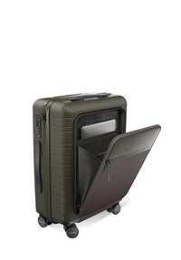 Valise rigide en vert olive, équipée de plusieurs roues, d'une surface texturée et d'une poche avant révélant un compartiment pour ordinateur portable.