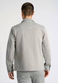 Grå långärmad skjorta med krage och knäppning vid ärmsluten. Slät, strukturerad tyg med modern passform och detalj på ryggen.