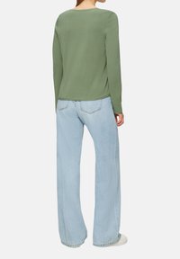 Zielony top z długim rękawem i okrągłym dekoltem, połączony z jasnoniebieskimi dżinsami o szerokich nogawkach. Miękki materiał i luźny krój. Proste detale przeszyć.