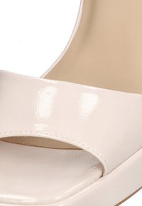 Sandalia de plataforma de charol crema con una amplia correa en el dedo del pie, diseño de punta abierta y un acabado suave y brillante.