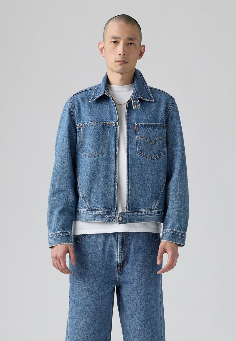 Giacca in denim di azzurro chiaro con design classico, due tasche sul petto, colletto a punta e dettagli di cucitura in vista.