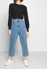 Top nero a coste a maniche lunghe con scollatura rotonda abbinato a jeans a vita alta azzurri e ampi, insieme a sneakers bianche.