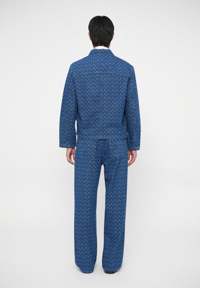 Conjunto de chaqueta y pantalones de mezclilla, con tela azul y un patrón repetido, corte holgado y detalles de costura visibles.
