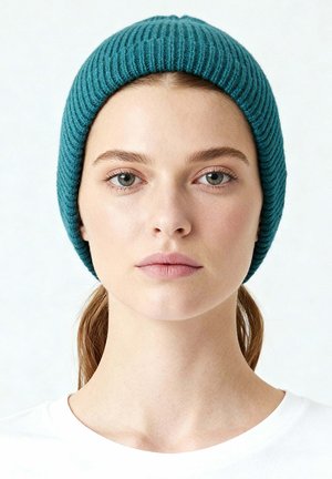 Cappellino a costine di colore verde acqua realizzato in materiale morbido, con vestibilità aderente e design semplice, indossato da una persona con i capelli lunghi.