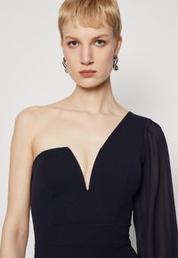 Robe navy avec un décolleté plongeant et une manche longue en voile. Le tissu semble lisse avec une coupe structurée et une taille définie.