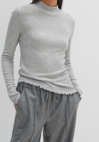 Grå ribbad långärmad topp med hög halsringning, som har en vågig fåll. Kombinerad med grå löst sittande byxor, vilket visar en avslappnad stil.