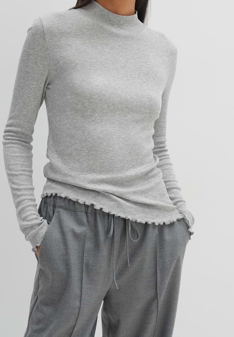 Grå ribbad långärmad topp med hög halsringning, som har en vågig fåll. Kombinerad med grå löst sittande byxor, vilket visar en avslappnad stil.