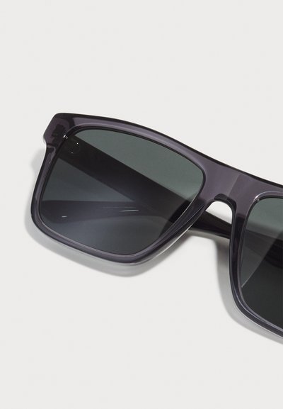 Ochelari de soare din plastic gri, cu o formă ușor unghiulară și lentile de un gri închis, având o suprafață netedă și un design minimalistic.