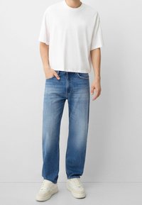 Camiseta de algodón blanca, de corte relajado. Pantalones vaqueros rectos de color azul claro con textura deslavada. Zapatillas de color crema con suelas texturizadas.