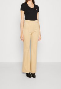Beige wijde broek met hoge taille, voorzien van voornaad en zakken, gecombineerd met een aansluitend zwart V-hals T-shirt en zwarte enkelboots.