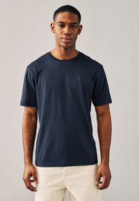 Marineblaues Baumwoll-T-Shirt mit Rundhalsausschnitt und kurzen Ärmeln; verfügt über ein kleines, gesticktes Logo auf der linken Brust. Einfaches, lässiges Design.