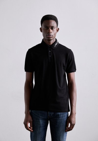 Zwarte polo met kraag, drie knopen en geborduurd detail op de kraag, gecombineerd met blauwe denim jeans.