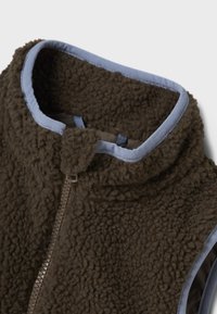 Fliisvest tumepruunis värvitoonis sinise äärega. Omadusteks kõrge krae ja täies ulatuses eesmine lukustus. Tekstuurse ja pehme materjaliga, luksusliku viimistlusega.