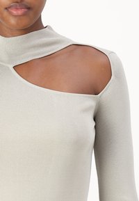Haut à manches longues côtelé gris clair avec un col montant et une découpe asymétrique à l'épaule. Texture douce et design ajusté.
