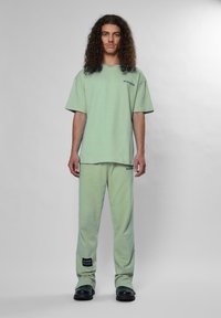 Világos zöld pamut póló, laza szabással, hozzátartozó, oldalsó címkével ellátott melegítőnadrággal. Mindkettő puha tapintású.