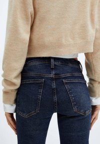 Pull court beige avec ourlet côtelé, associé à un jean denim bleu foncé avec jambes droites et poches arrière à couture subtile.