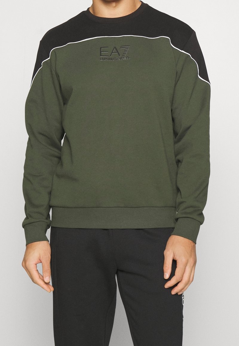 Felpa verde oliva con yoke nero, piping bianco e logo in rilievo sul petto. I polsini e l'orlo a costine conferiscono struttura.