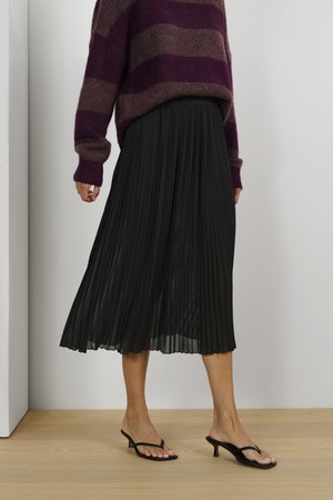 Schwarzer, plissierter Midirock mit fließendem Design, kombiniert mit einem burgunderfarbenen und braun gestreiften Pullover sowie schwarzen, hohen Flip-Flops.