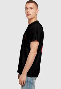 Sort bomulds t-shirt med rund hals og korte ærmer; har et lille pink logo på fronten og et større pink design på bagsiden.