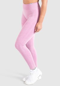 Leggings rosa con vita alta, tessuto testurizzato e dettagli a costine lungo i lati, abbinati a scarpe da ginnastica bianche.