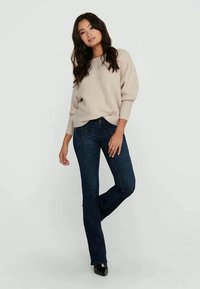Beige textured sweater with loose fit, paired with dark blue flared jeans. Model stands on a plain background, showcasing both garments.