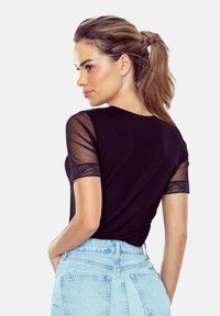 Czarny t-shirt z krótkimi, przezroczystymi, siateczkowymi rękawami i koronkowym wykończeniem. Posiada klasyczny okrągły dekolt oraz dopasowany krój, zestawiony z jasnoniebieskimi dżinsami.