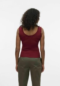 Top de tirantes burdeos con detalles acanalados, escote redondeado y volantes en los tirantes, combinado con pantalones verde olivo.