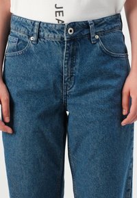 Μπλε τζιν παντελόνι με ψηλή μέση, σχέδιο ίσιας πόδας και κλασικό στυλ πέντε τσεπών. Διαθέτει μεταλλικές λεπτομέρειες και διακριτική φθορά.